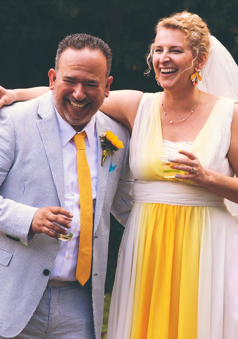 Bride and groom, arms around each other laughing after being married.
