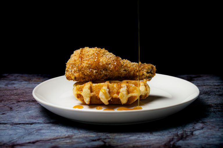 Chicken and waffles on a white plate, marble table and a black background.