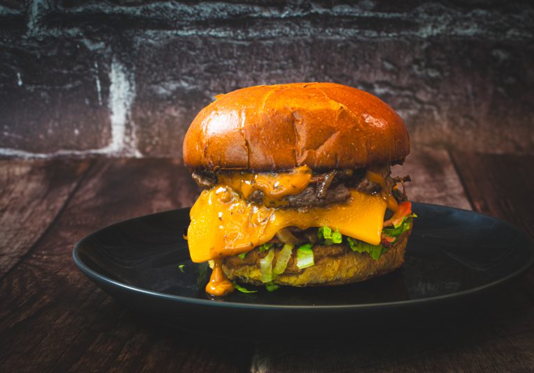 Double cheese burger with lettuce and tomato on a brioche bun sitting on a wood table with a brick background