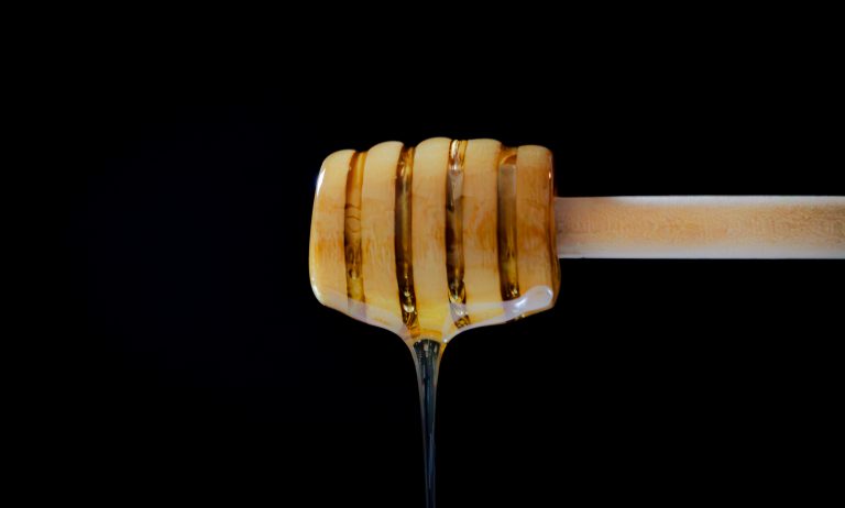 Honey dipper with a black background drizzling honey